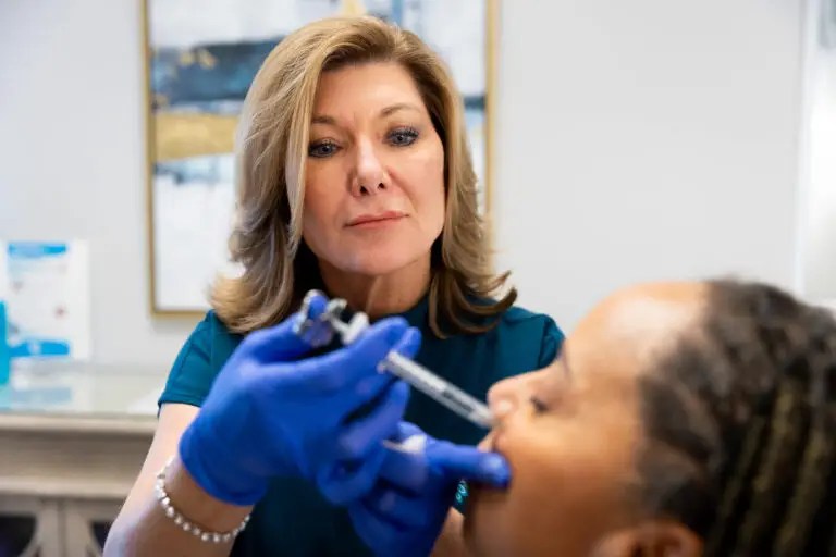 A medical professional with blue gloves injects a female patient's cheek with dermal filler in Greensboro, NC