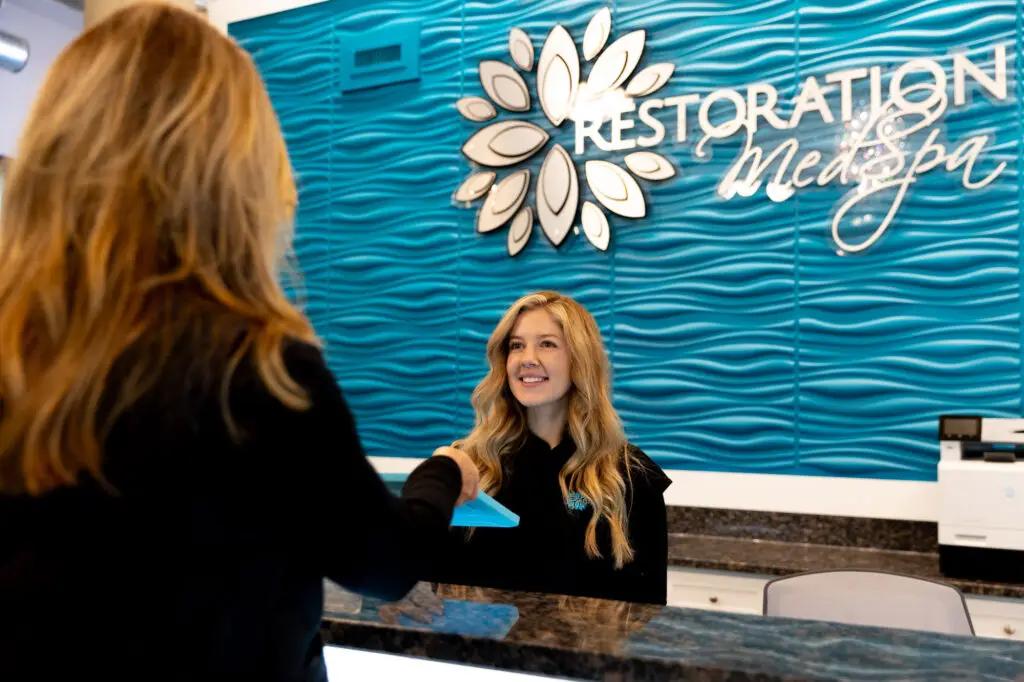 a front desk employee smiles while signing a patient in for an appointment for medical weight loss in Greensboro