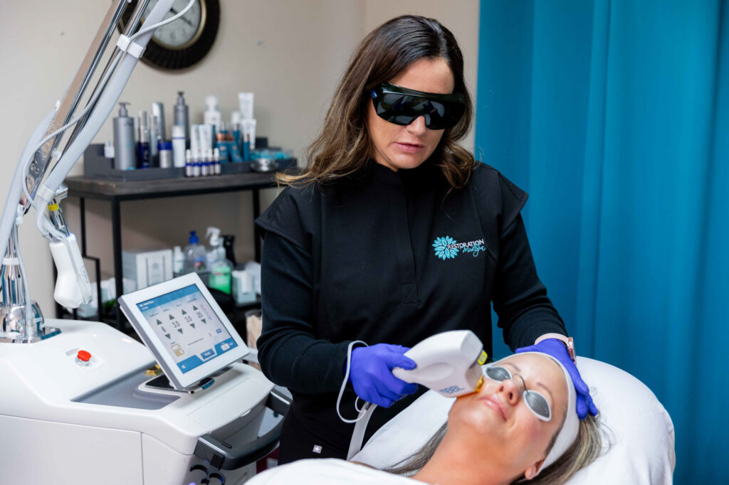 A female Restoration MedSpa provider uses a BBL laser in Greensboro on a female patient. Both women are wearing protective eyewear.
