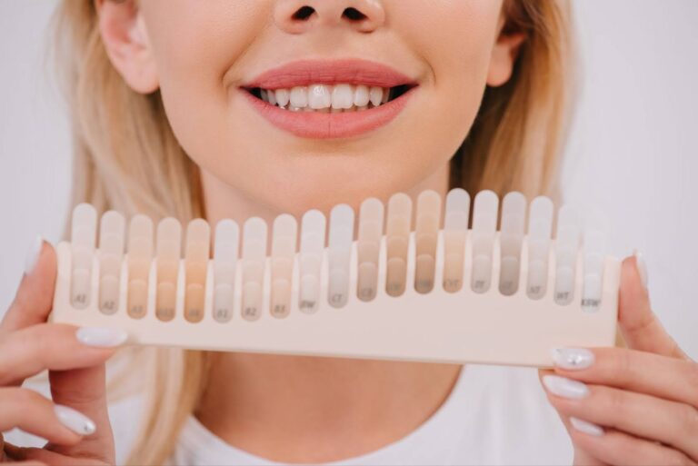 A woman smiles while holding a teeth whitening shade display after completing teeth whitening near High Point, NC