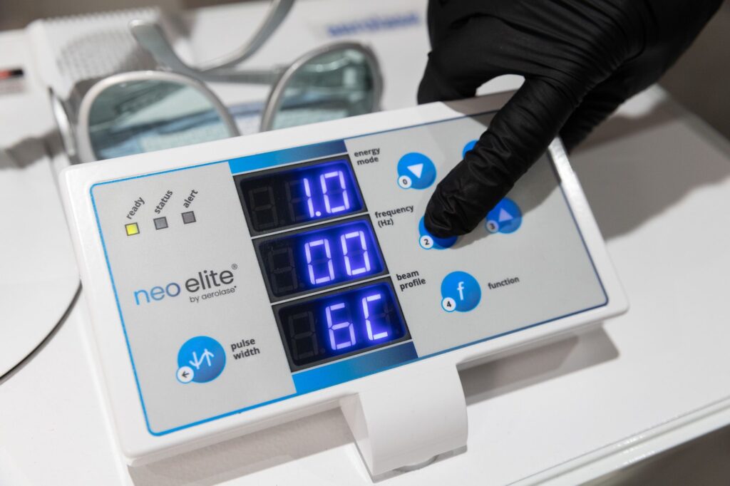 A Restoration MedSpa provider wearing black gloves pushes buttons to adjust the energy mode, frequency, function, and pulse width on the Aerolase NeoElite, an Aerolase laser in Greensboro.