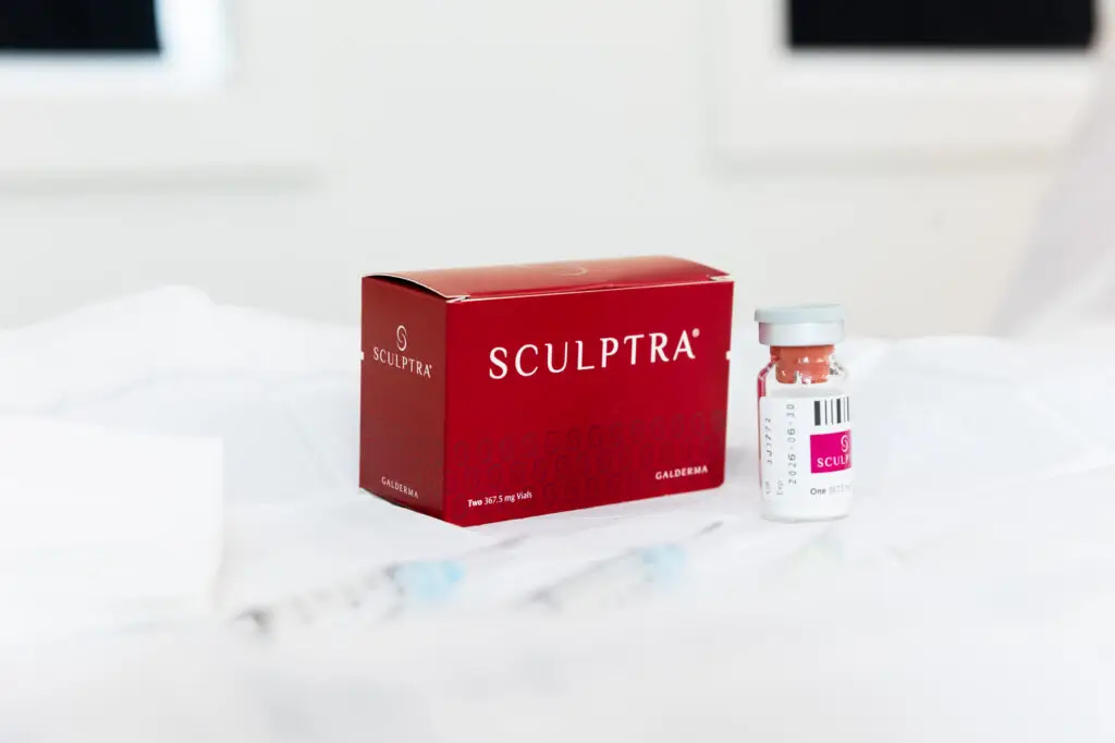A box of Sculptra injections in Winston-Salem, accompanied by an unopened vial and two empty needles, sit on a small table. This cosmetic injectable restores skin health from the inside out.