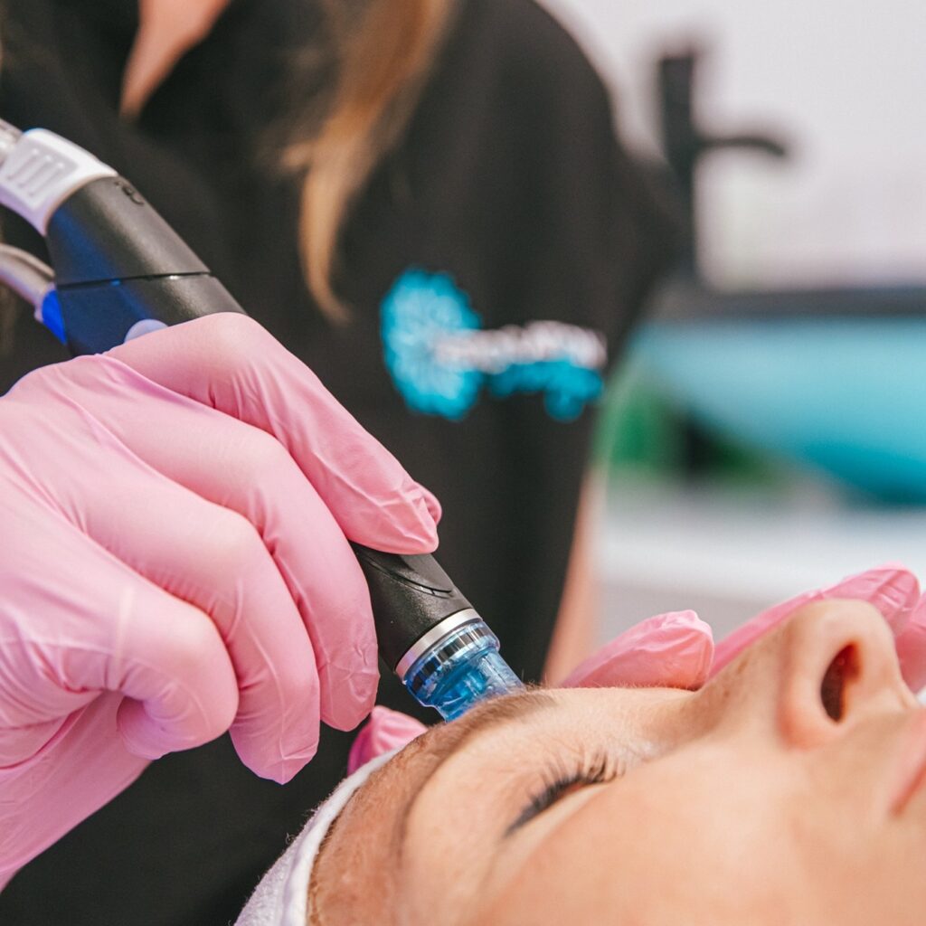 A Restoration MedSpa medical provider wearing pink gloves conducts a Hydrafacial on a female client. The treatment for skin rejuvenation in Greensboro thoroughly cleanses and hydrates the skin.
