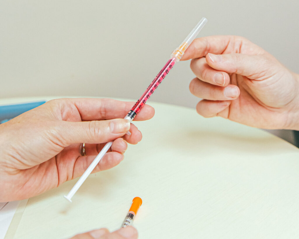 A female Restoration MedSpa provider, wearing silver rings on two of her fingers, shows a client a filled syringe of weight loss injections at our weight loss clinic in Winston-Salem. This medication manages blood sugar and slows digestion, and is a sustainable weight loss strategy.