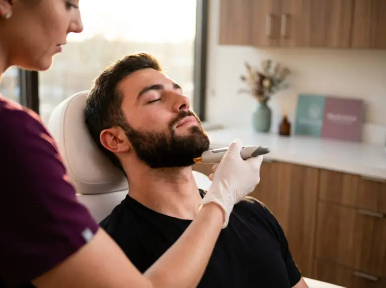 Male client receives laser hair removal along the beard line in a bright medspa treatment room, while a provider in scrubs performs the procedure with gentle precision and care.